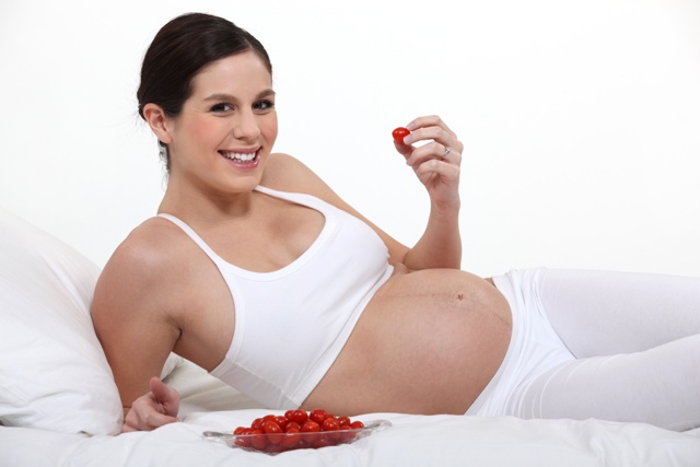 A pregnant woman eating strawberries on her bed.